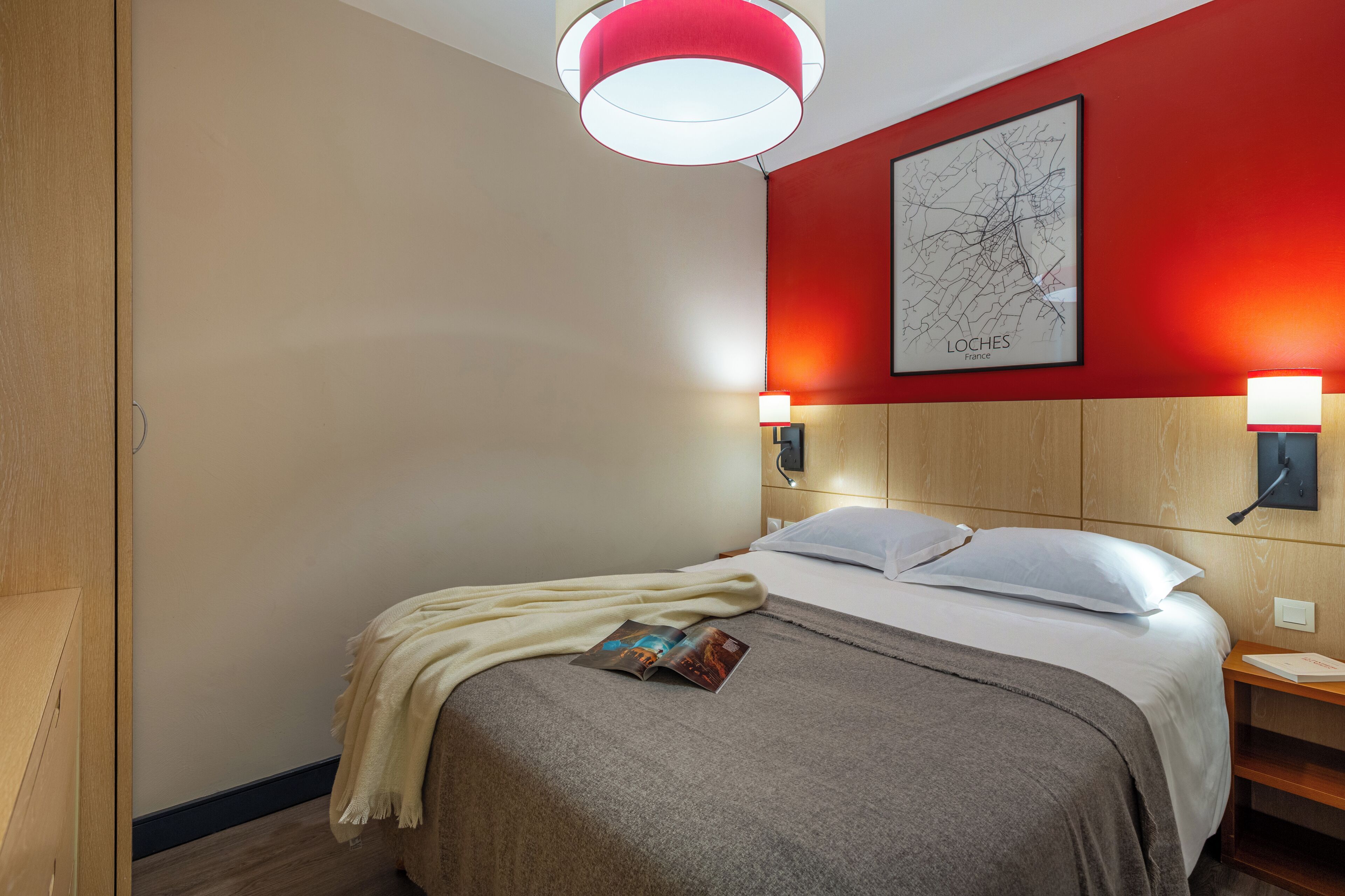 Ein Hotelzimmer mit Bett, einer roten Akzentwand, einer Karte und einer Zeitschrift auf dem Bett.