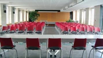 A conference room with rows of red chairs and a long table, large windows, and a ceiling with recessed lighting.