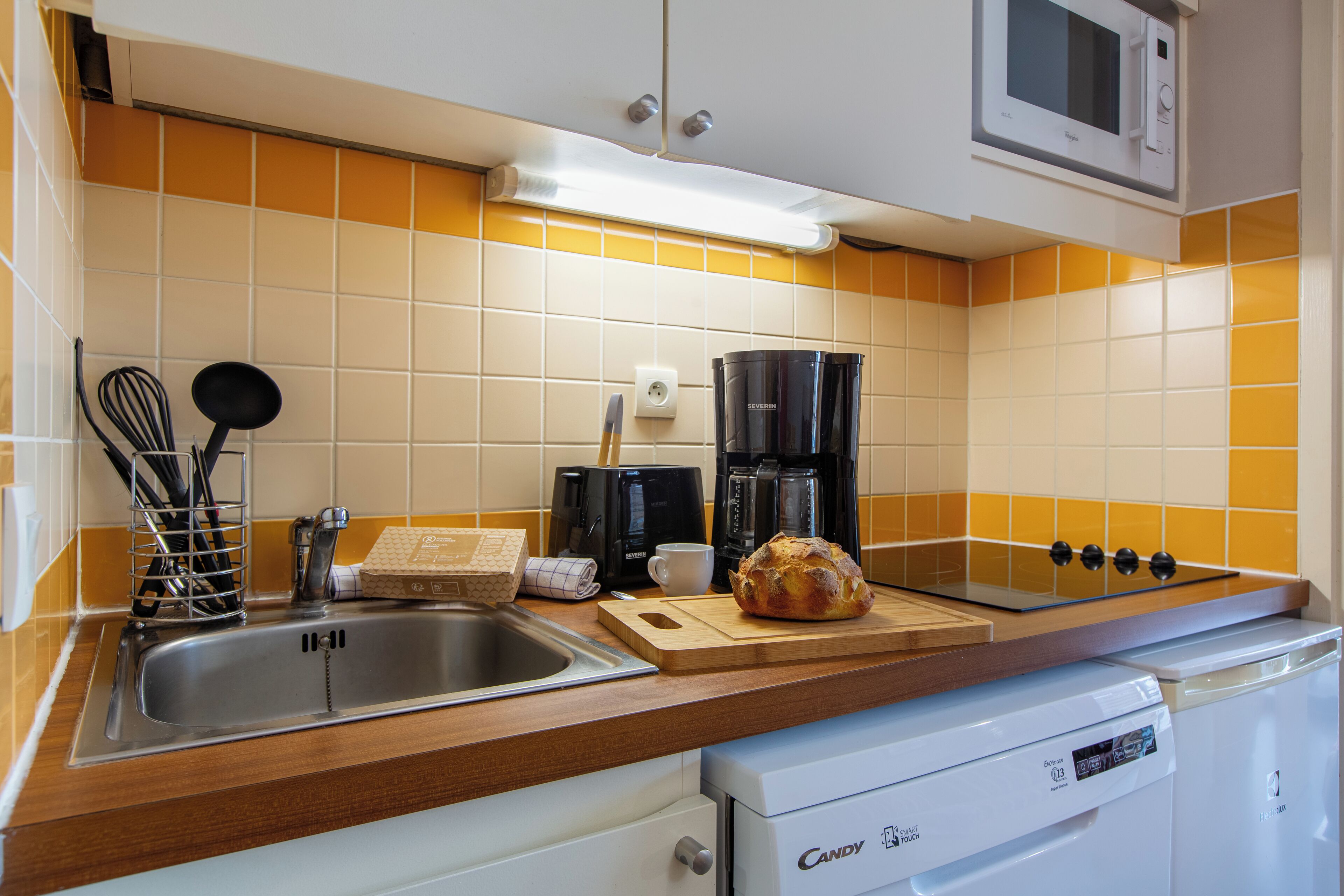 A kitchen with a sink, a coffee maker, a toaster, and a loaf of bread on the counter.