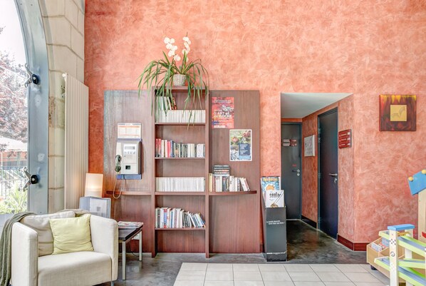 A cozy lobby with a bookshelf, a couch, a radiator, and a door leading to another room.
