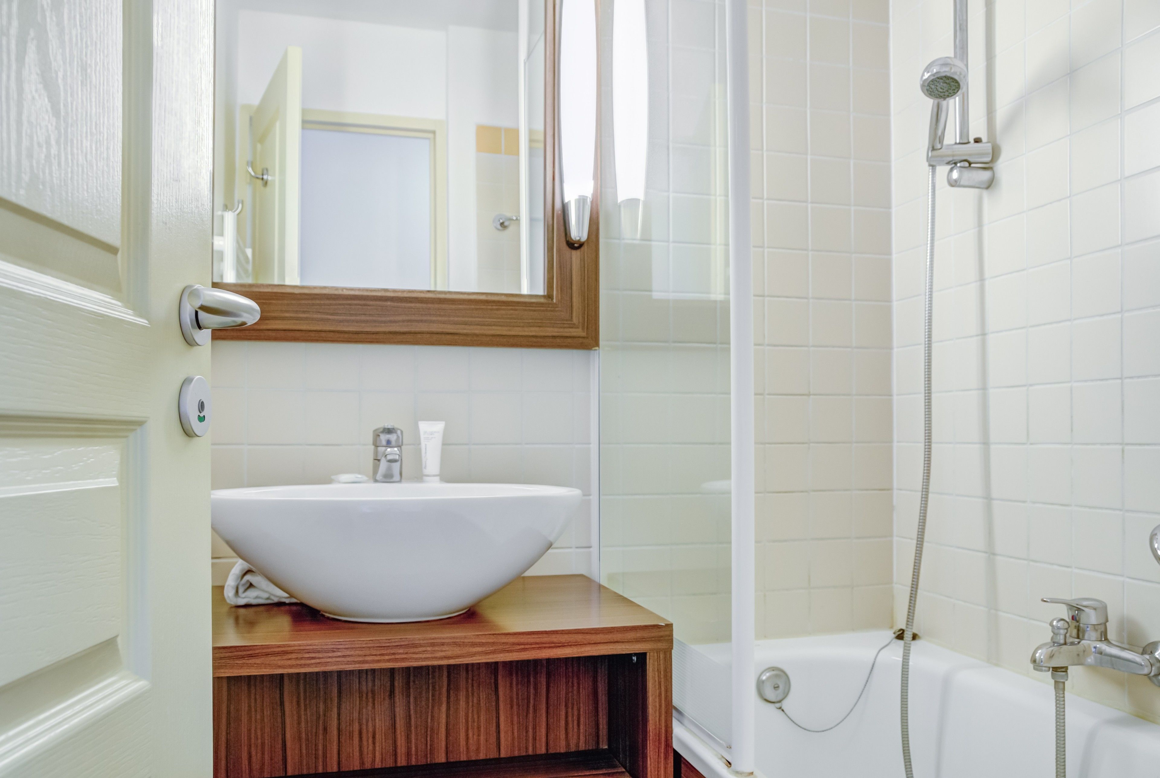 Un baño con un lavabo blanco, tocador de madera, un espejo y zona de ducha.