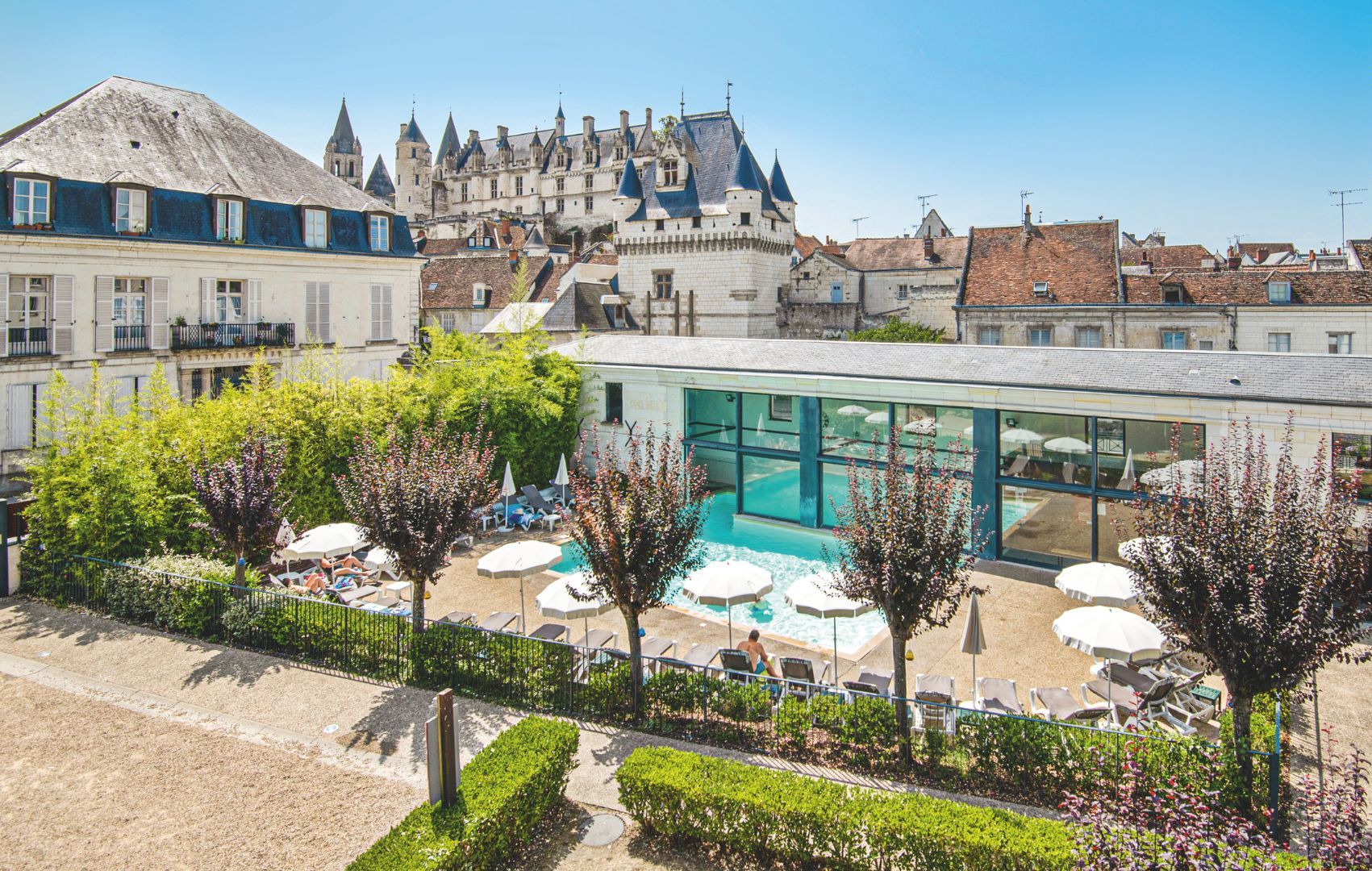 Een hotel met een zwembad, omringd door ligbedden en parasols, met een kasteel op de achtergrond.