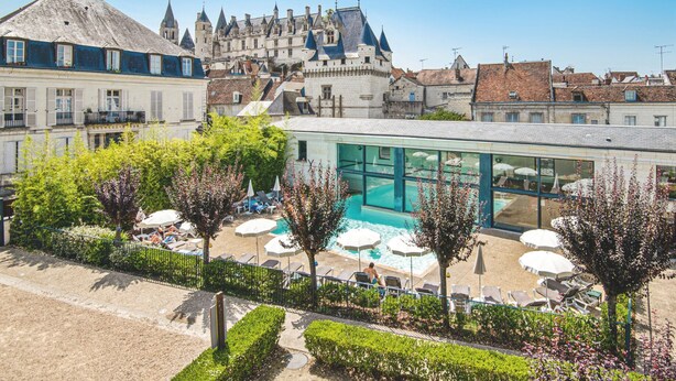Un hotel con piscina, rodeado de sillones de descanso y sombrillas, con un castillo al fondo.