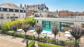 Een hotel met een zwembad, omringd door ligbedden en parasols, met een kasteel op de achtergrond.