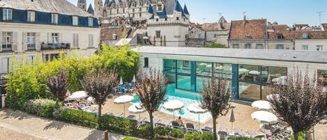 Ein Hotel mit Schwimmbad, umgeben von Liegestühlen und Sonnenschirmen, mit einer Burg im Hintergrund.