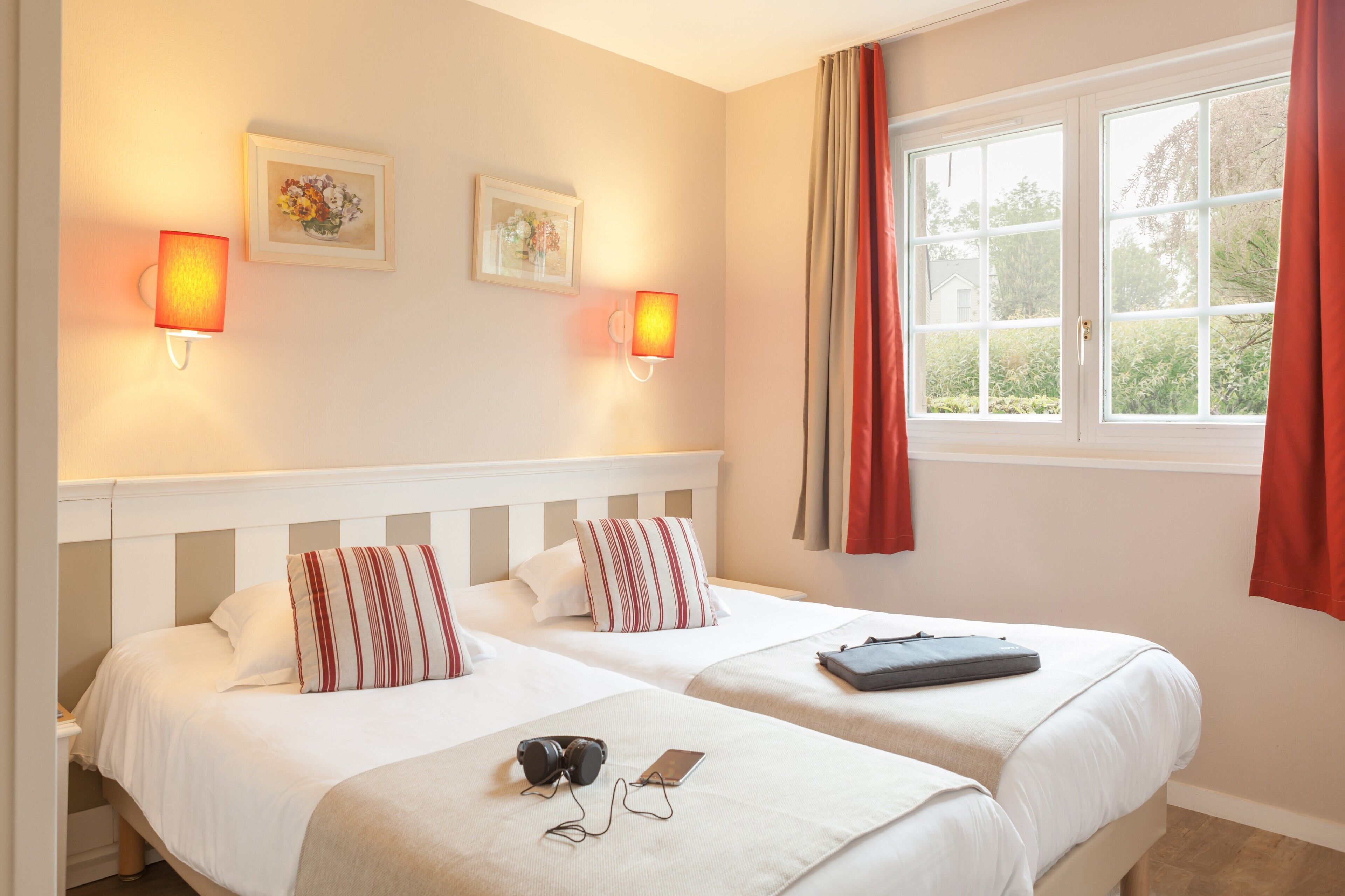 Habitación de hotel con dos camas, una ventana con cortinas rojas y lámparas fijadas a la pared.