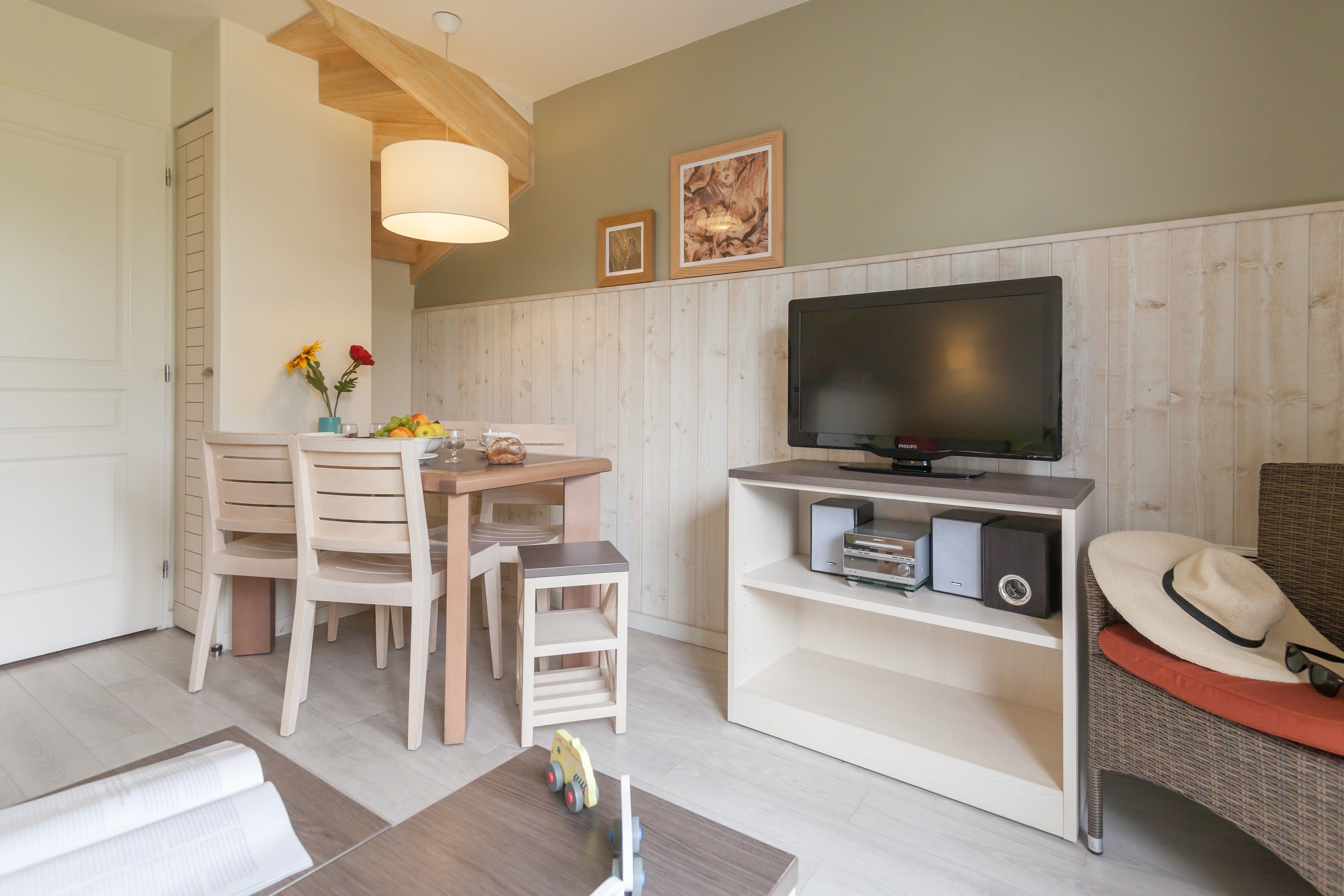 Un salon comprenant une table à manger en bois, des chaises, un téléviseur posé sur un meuble et une bibliothèque.
