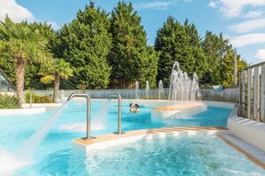 Une piscine dotée de plusieurs éléments aquatiques décoratifs, entourée d’une clôture en bois et d’une végétation luxuriante.