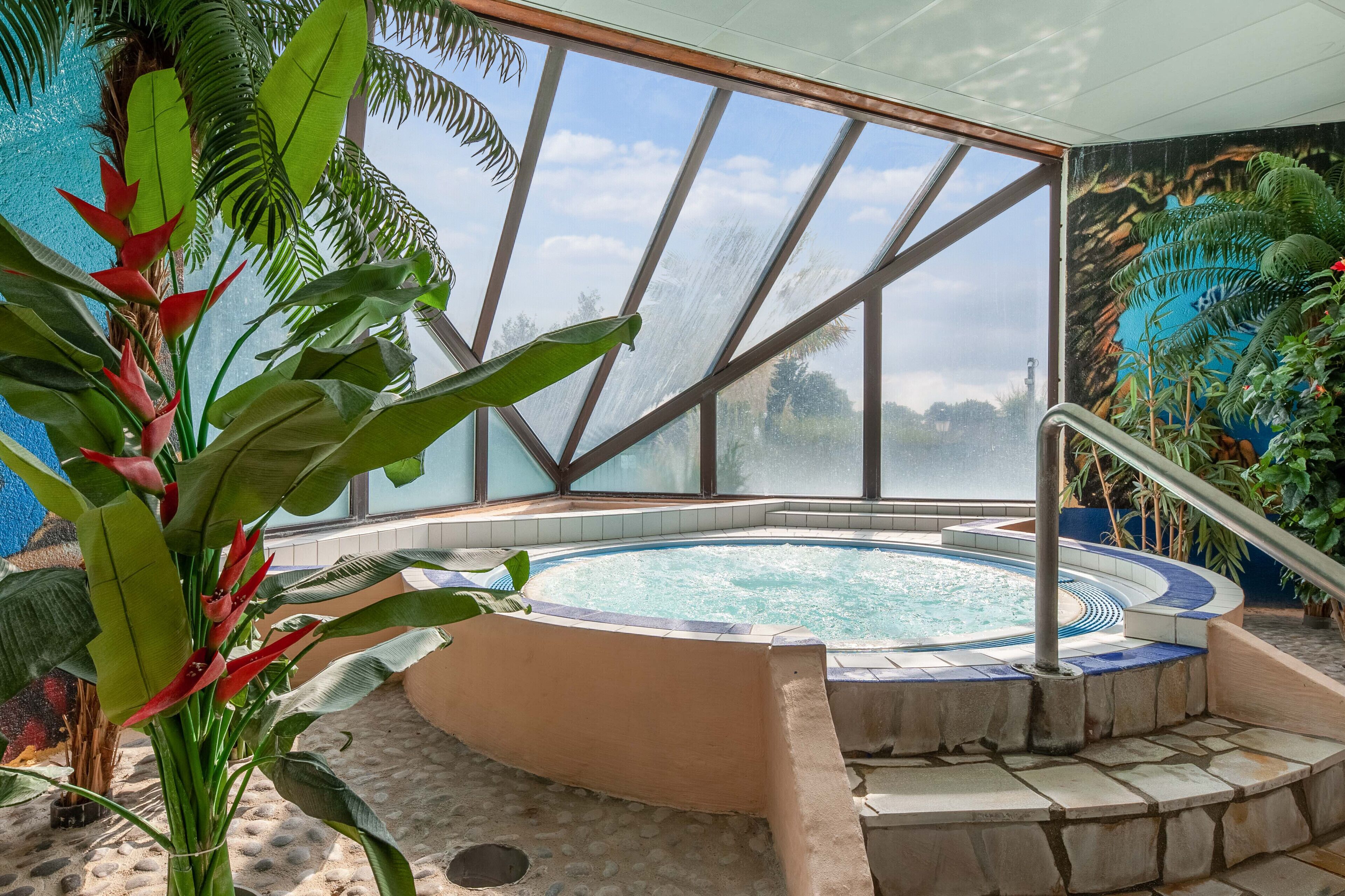 Un bain à remous entouré de pierres, bordé de plantes tropicales et doté d’une grande fenêtre.