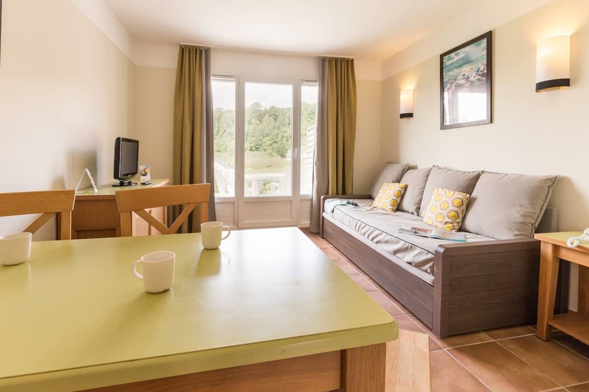 Een kamer met een eettafel, stoelen, een bank met patroon kussens, een televisie en een raam met gordijnen.