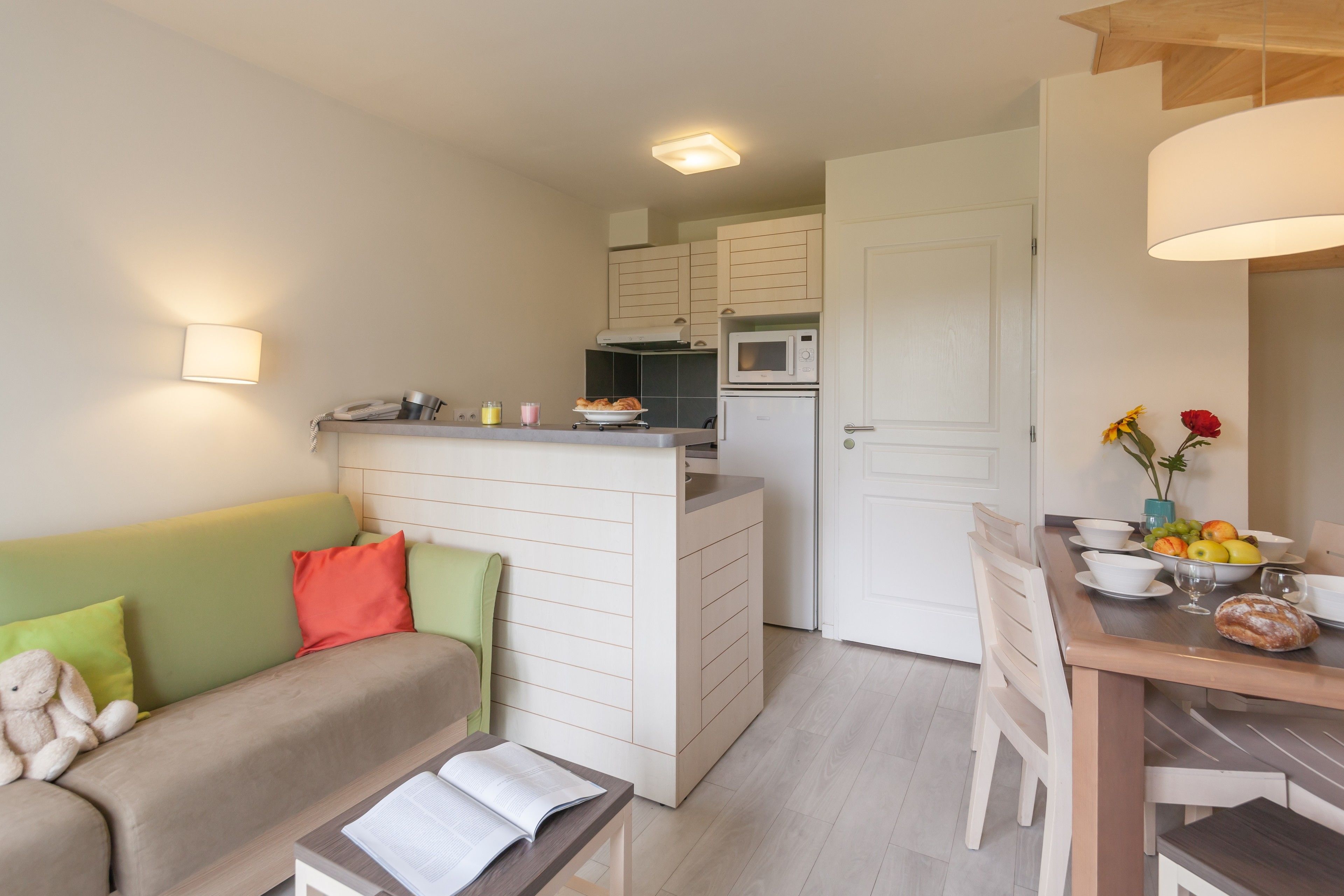 En kompakt bolig med tekøkken, spiseplads og sofa med hynder.
