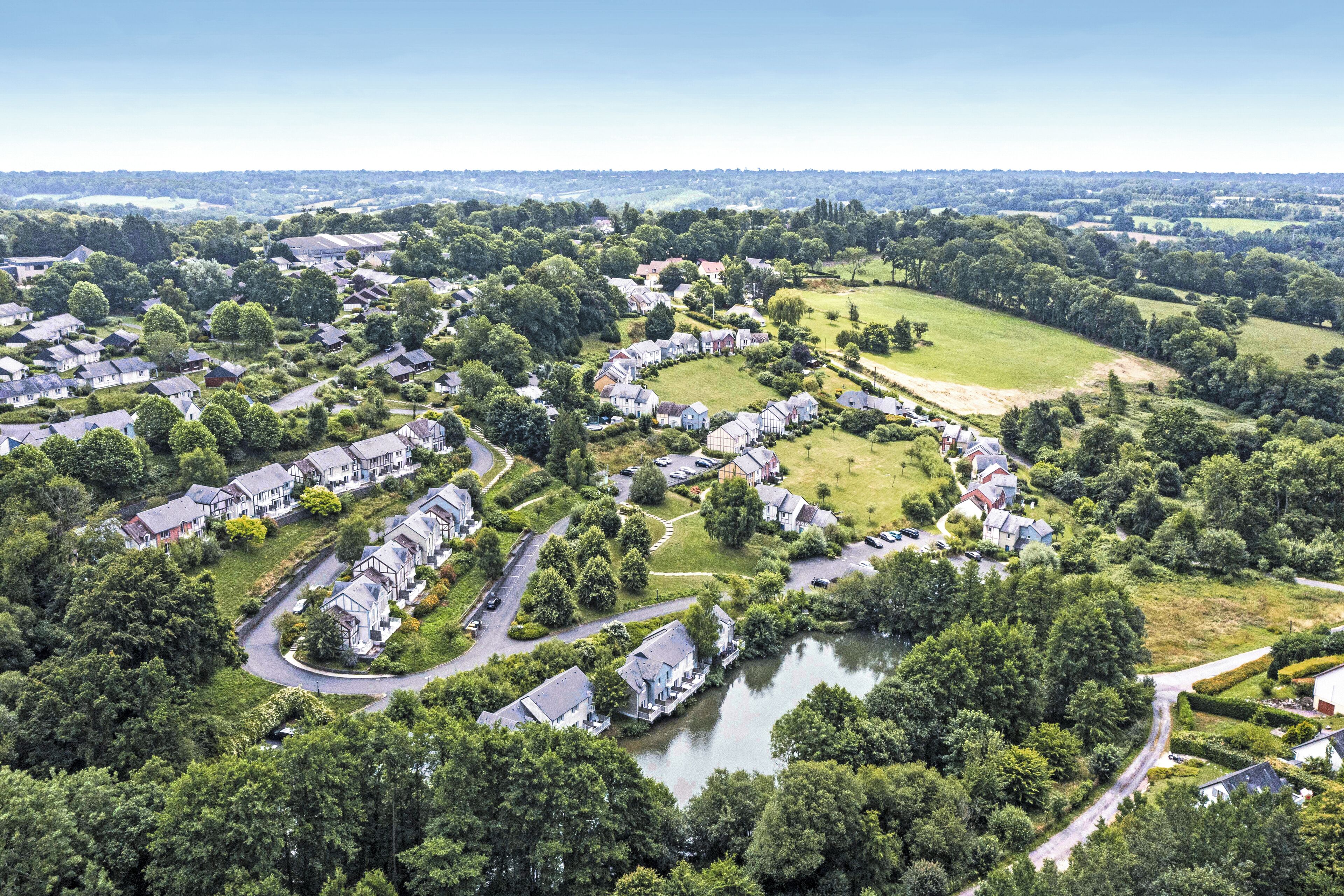An aerial view of a residential area with houses, a lake, and surrounding greenery.