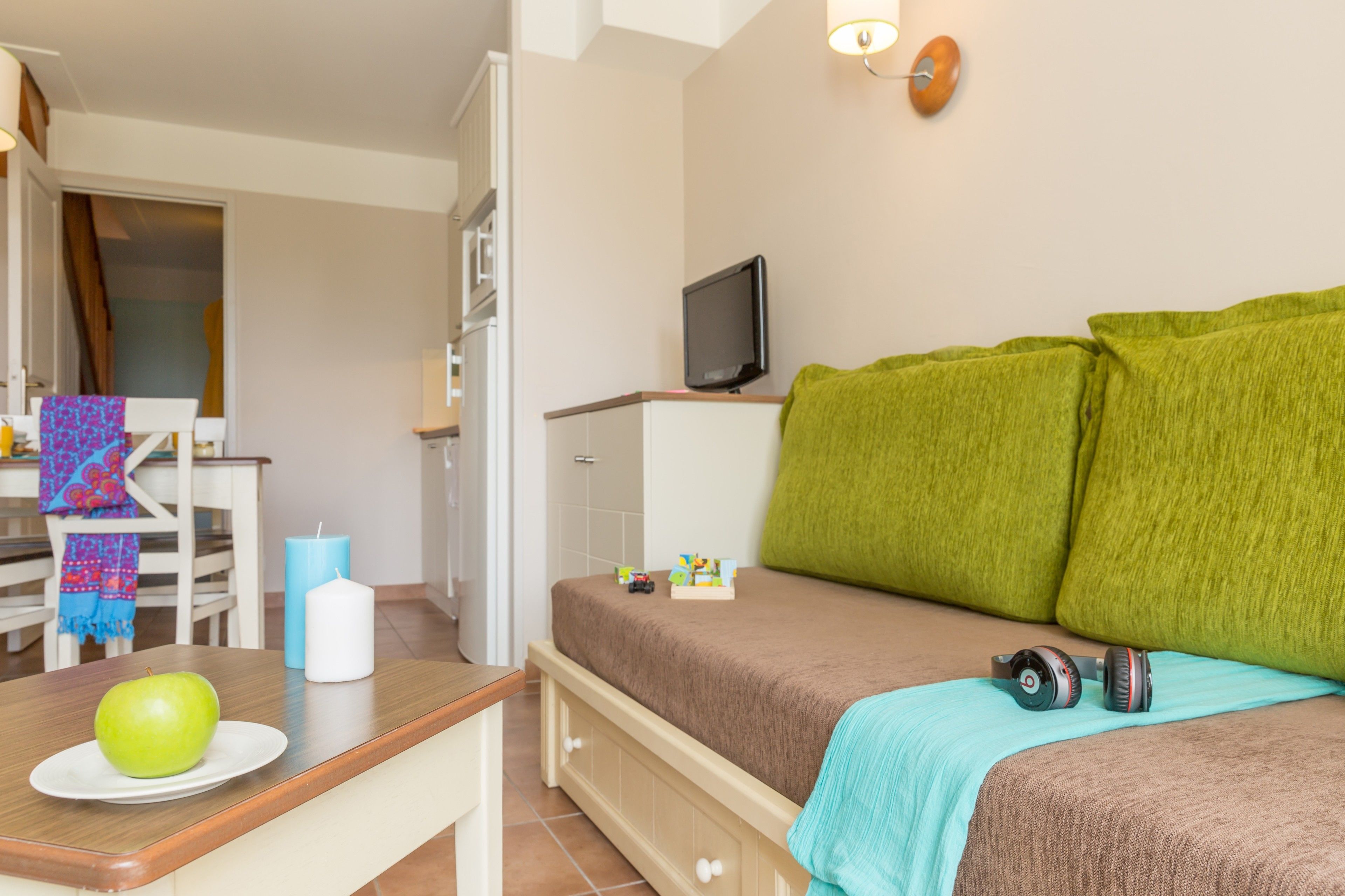 Un dormitorio con una cama, un televisor, una mesa con una manzana y una vela azul.
