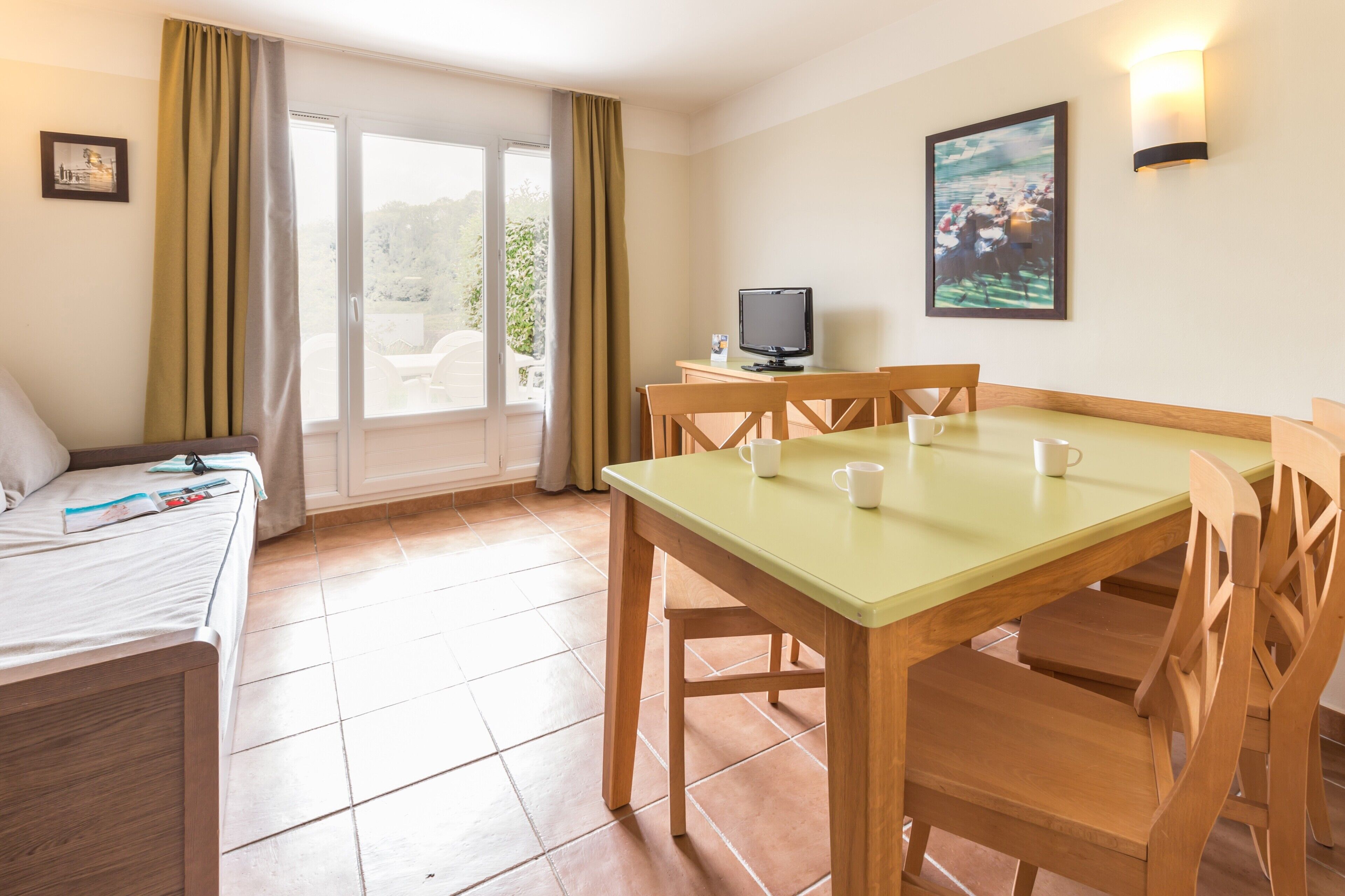 A hotel room with a bed, a dining table with chairs, a TV, and a balcony with curtains.