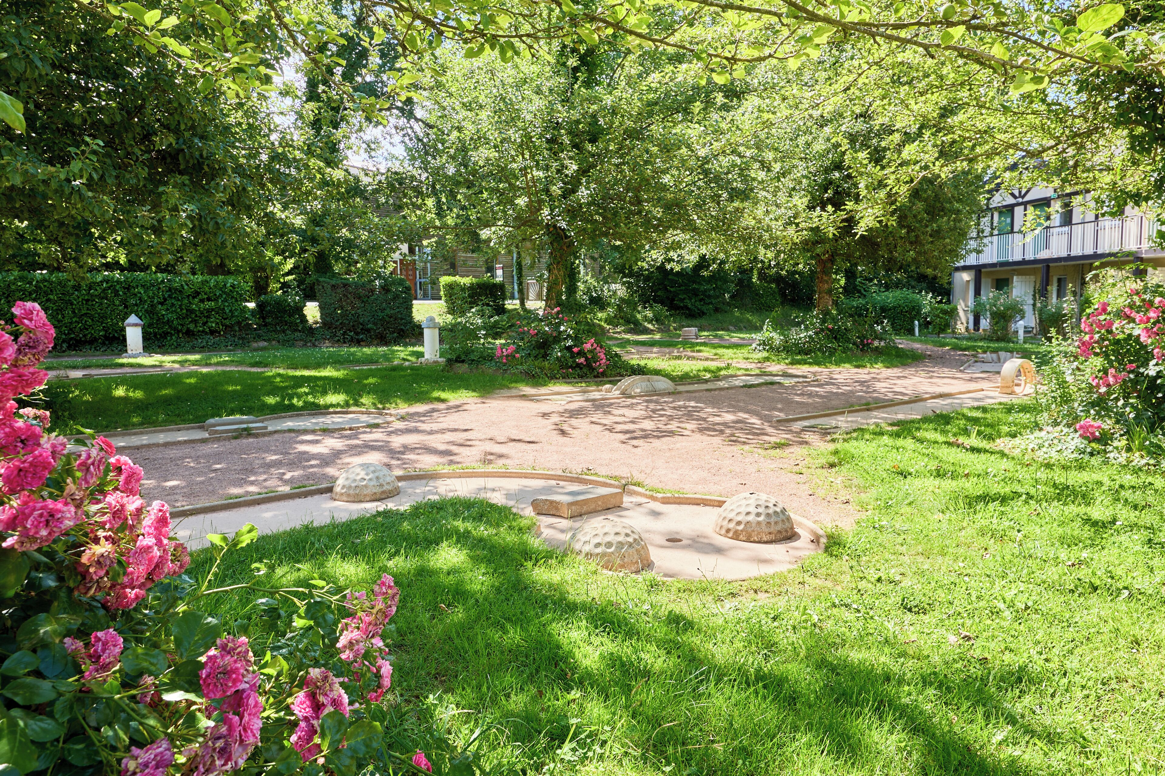 A garden with a paved path, a white gazebo, and a building with a balcony.