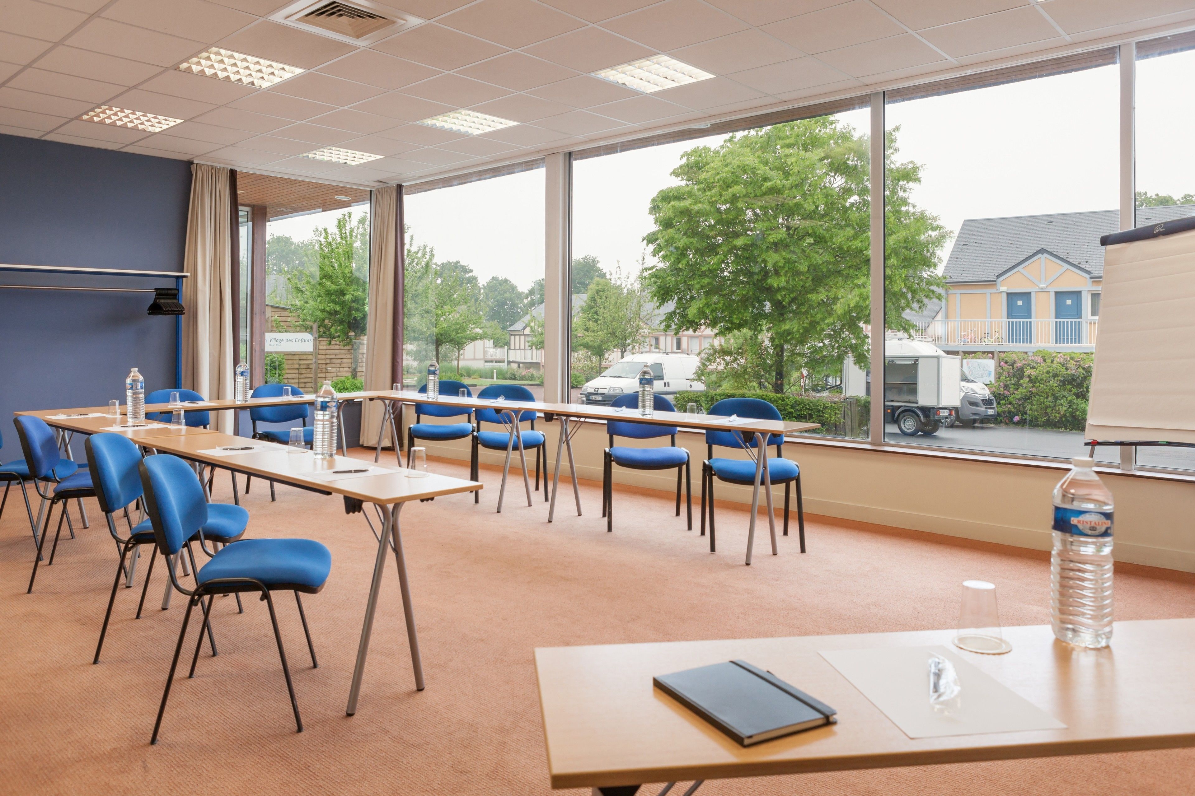 A conference room with tables and chairs, large windows with a view of a street and buildings, and a water bottle on a table.