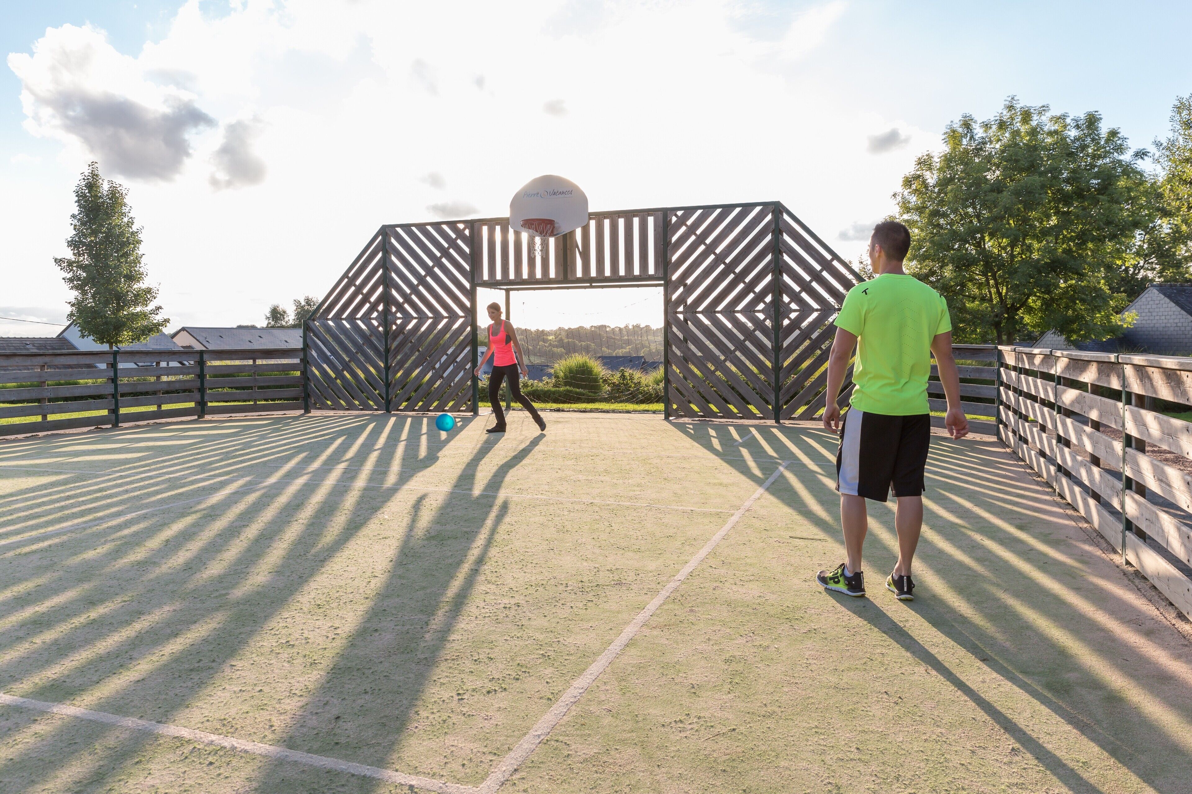 An outdoor basketball court with a wooden fence and a basketball hoop.