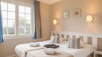 A hotel room with two beds, a window with curtains, wall-mounted lights, and framed pictures.
