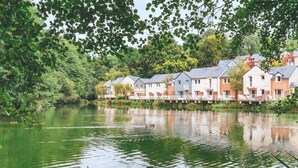 A row of houses by a calm lake, surrounded by lush greenery. - Village Normandy Garden Pierre & Vacances (Branville)