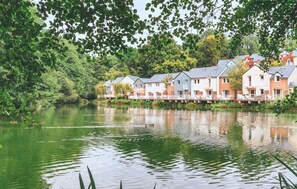 A row of houses by a calm lake, surrounded by lush greenery. - Village Normandy Garden Pierre & Vacances (Branville)