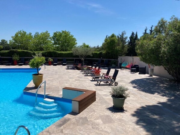 Un área de piscina con una piscina azul cristalina, sillas de descanso y plantas en macetas.
