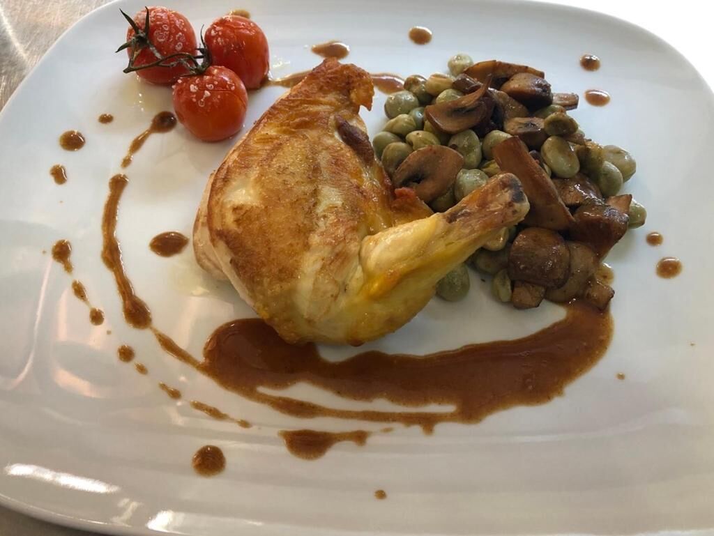A plate with a roasted chicken leg, cherry tomatoes, and mushrooms.