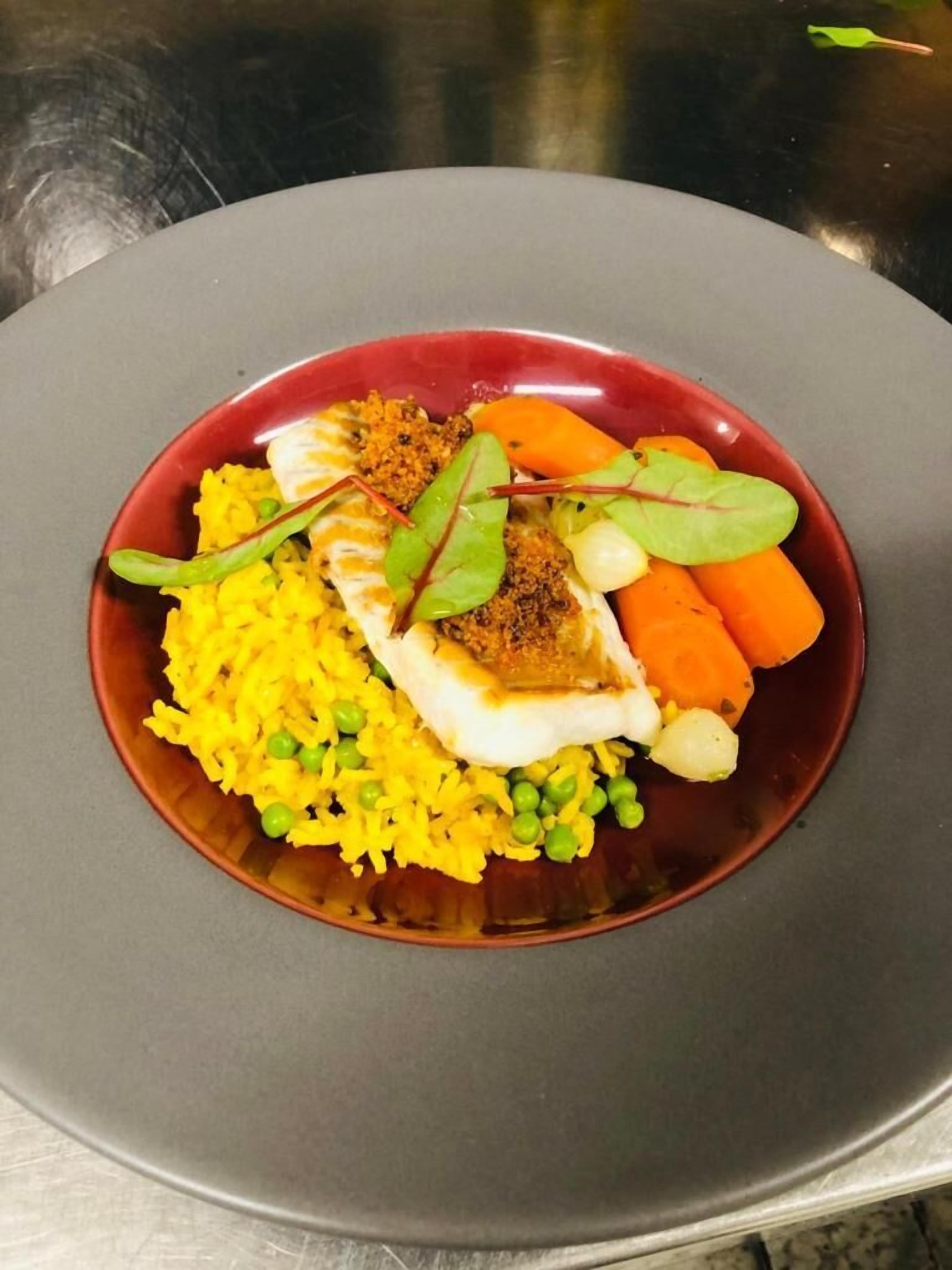 Un plato de comida con arroz, guisantes, zanahorias y un trozo de pescado, servido en un plato rojo.