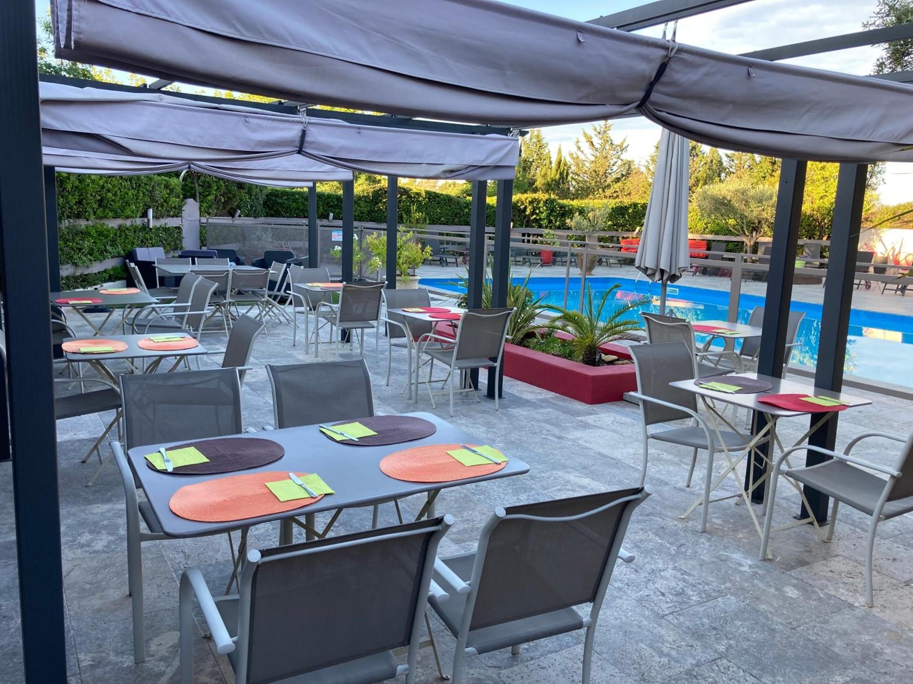 An outdoor patio area with tables and chairs, a pool, and a covered seating area.