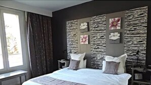 A modern bedroom with a large bed, stone wall decor, and a window with curtains. - Logis Hôtel les Aubuns Country Hôtel (Saint-Gilles)