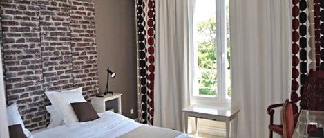 Hotelkamer met een bakstenen muur, een groot bed met witte beddengoed, een bureau met stoel en een raam met gordijnen.