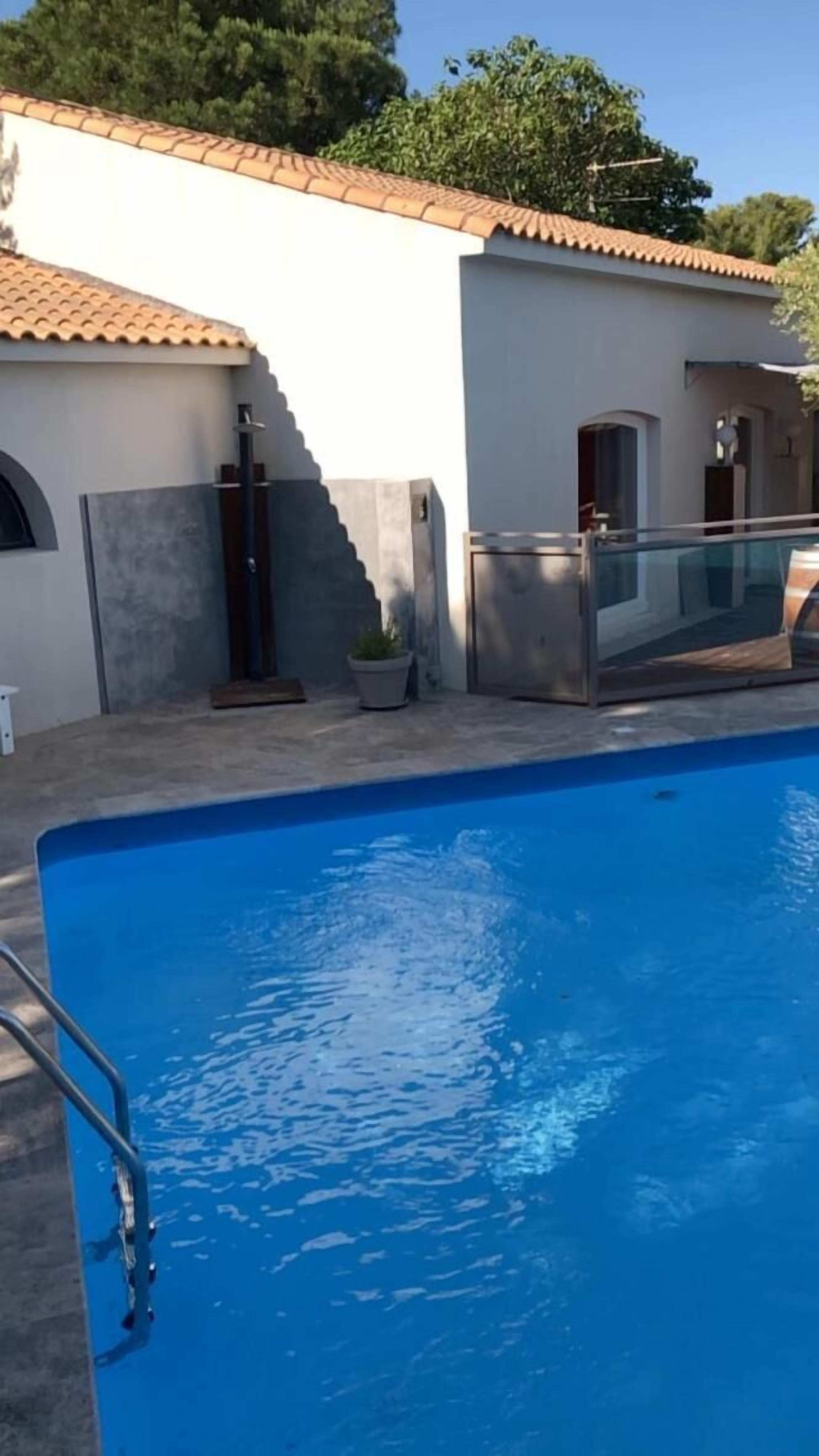 Una piscina con superficie de agua azul cristalina, rodeada por un edificio blanco con tejado de baldosas y una pequeña planta en maceta.