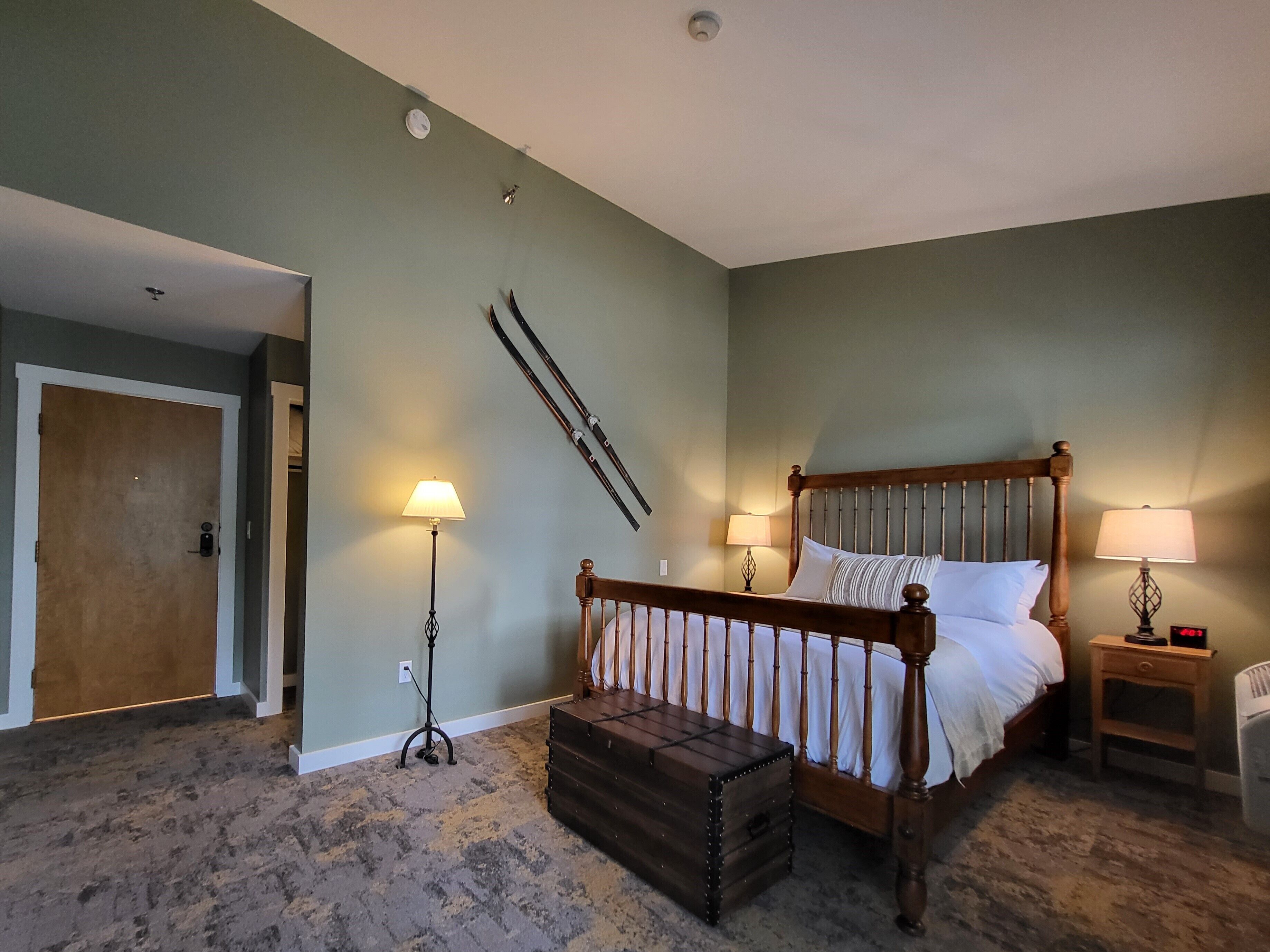 Une chambre avec un lit en bois, deux lampes de chevet, une table de nuit, une commode en bois et une paire de skis appuyés contre le mur.