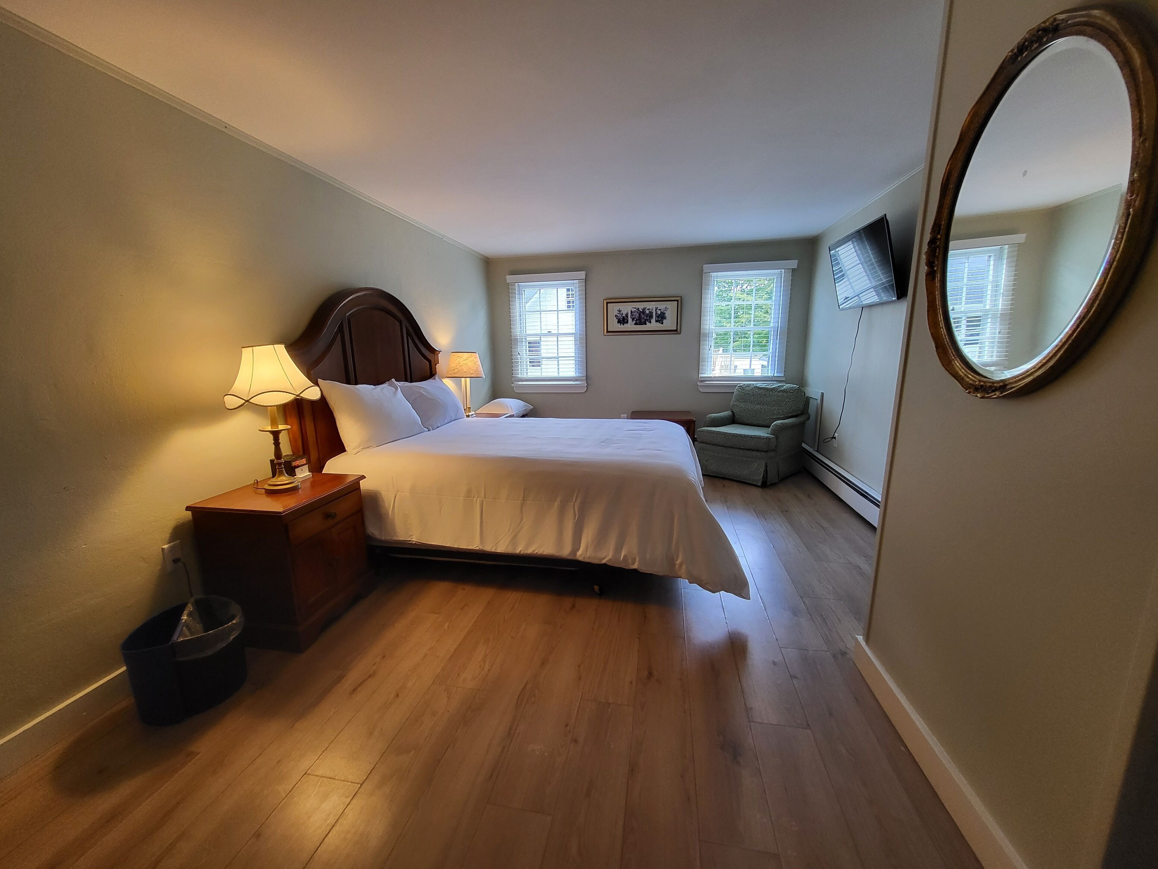 A bedroom with a bed, two bedside tables, a chair, a TV, and two windows.
