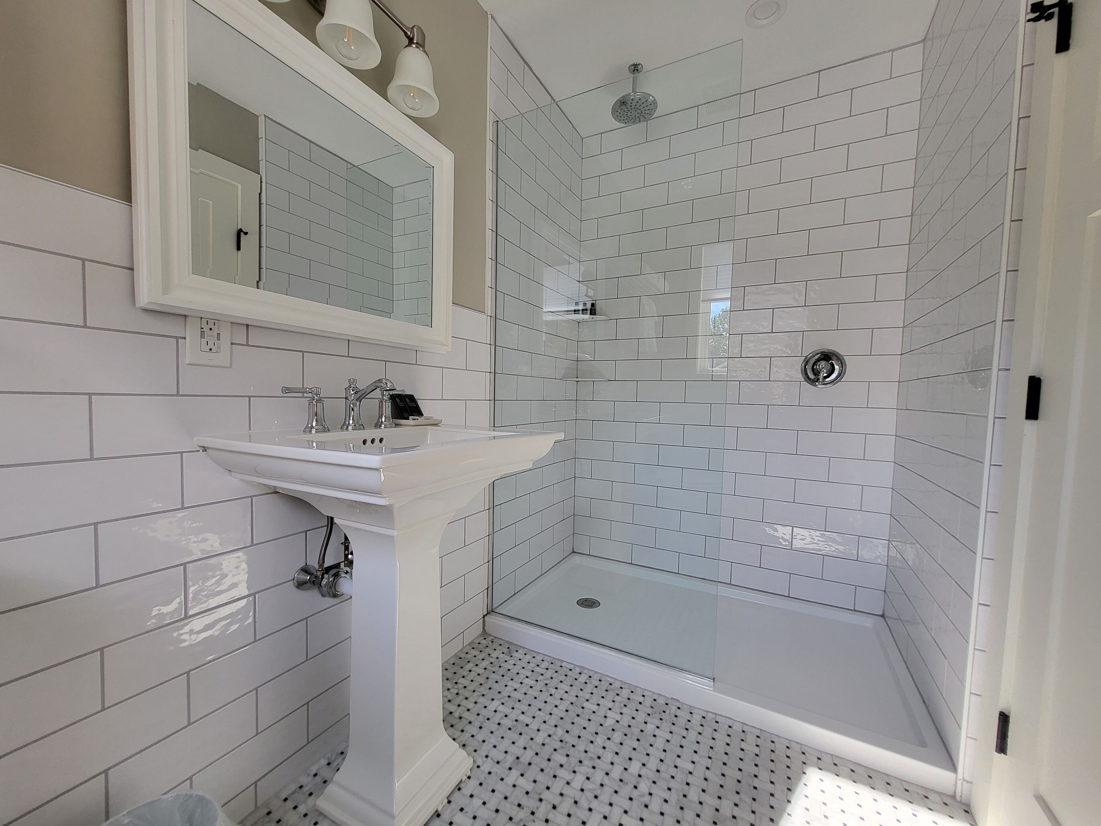 A modern bathroom with a glass-enclosed shower, a pedestal sink, and a large mirror above the sink.