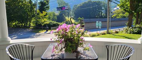 Eine überdachte Terrasse mit Tisch und zwei Stühlen, die auf eine Straße mit Verkehrsschildern und ein Gebäude in der Ferne blickt.