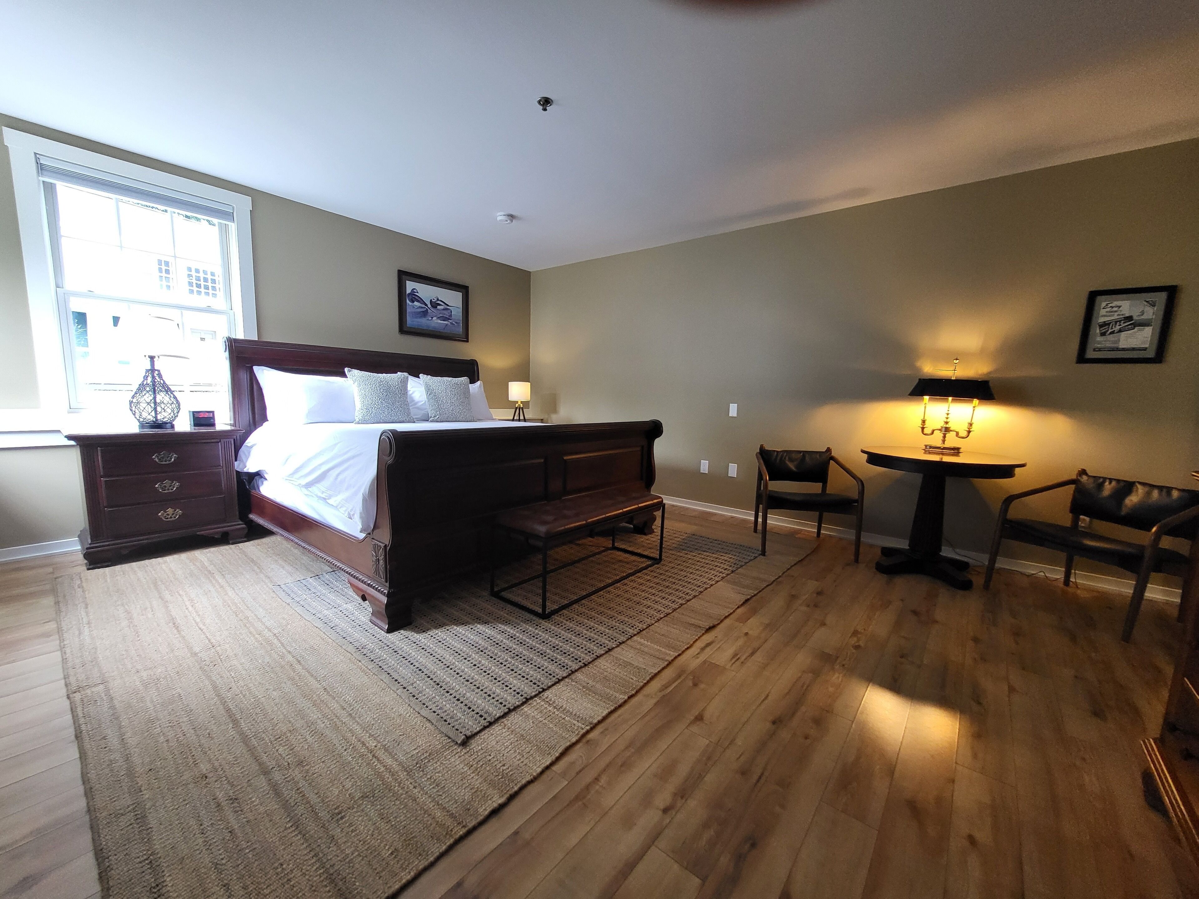 A bedroom with a large bed, a bedside table with a lamp, a chair, and a small table with a lamp.