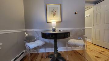 A dining area with a round table, two chairs, a framed picture on the wall, and a lamp.