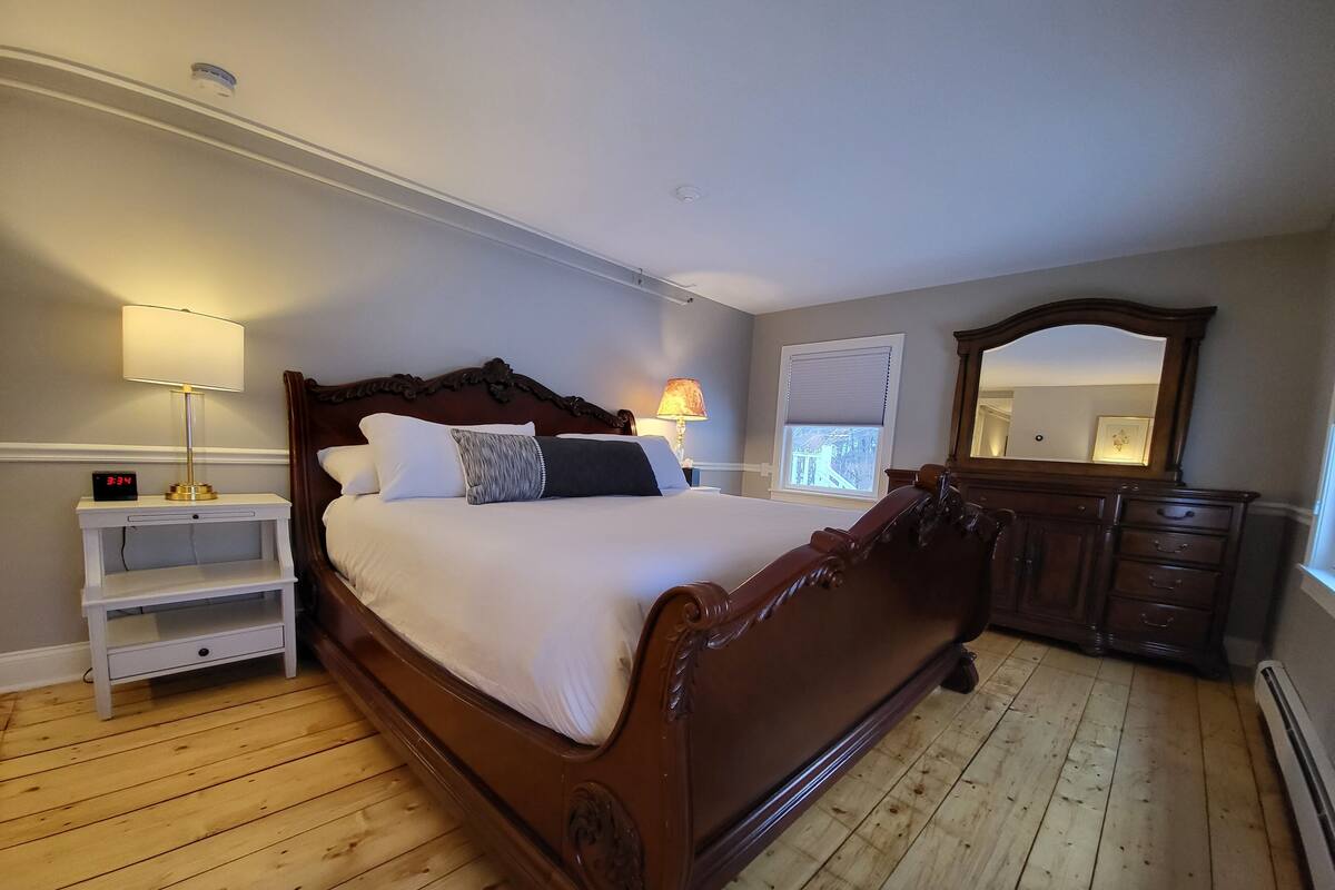A neatly arranged bedroom with a large bed, bedside tables, a dresser, and a mirror.