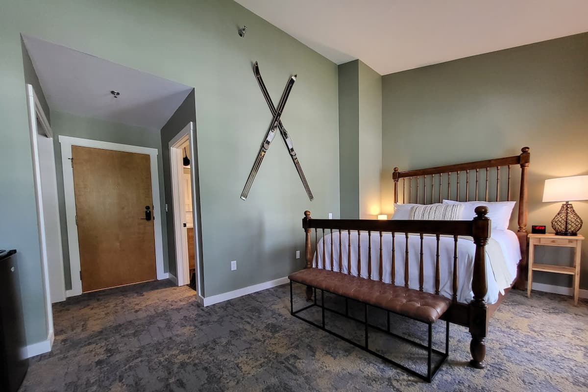 A bedroom with a wooden bed, a bench, a wall-mounted ski rack, and a nightstand with a lamp.