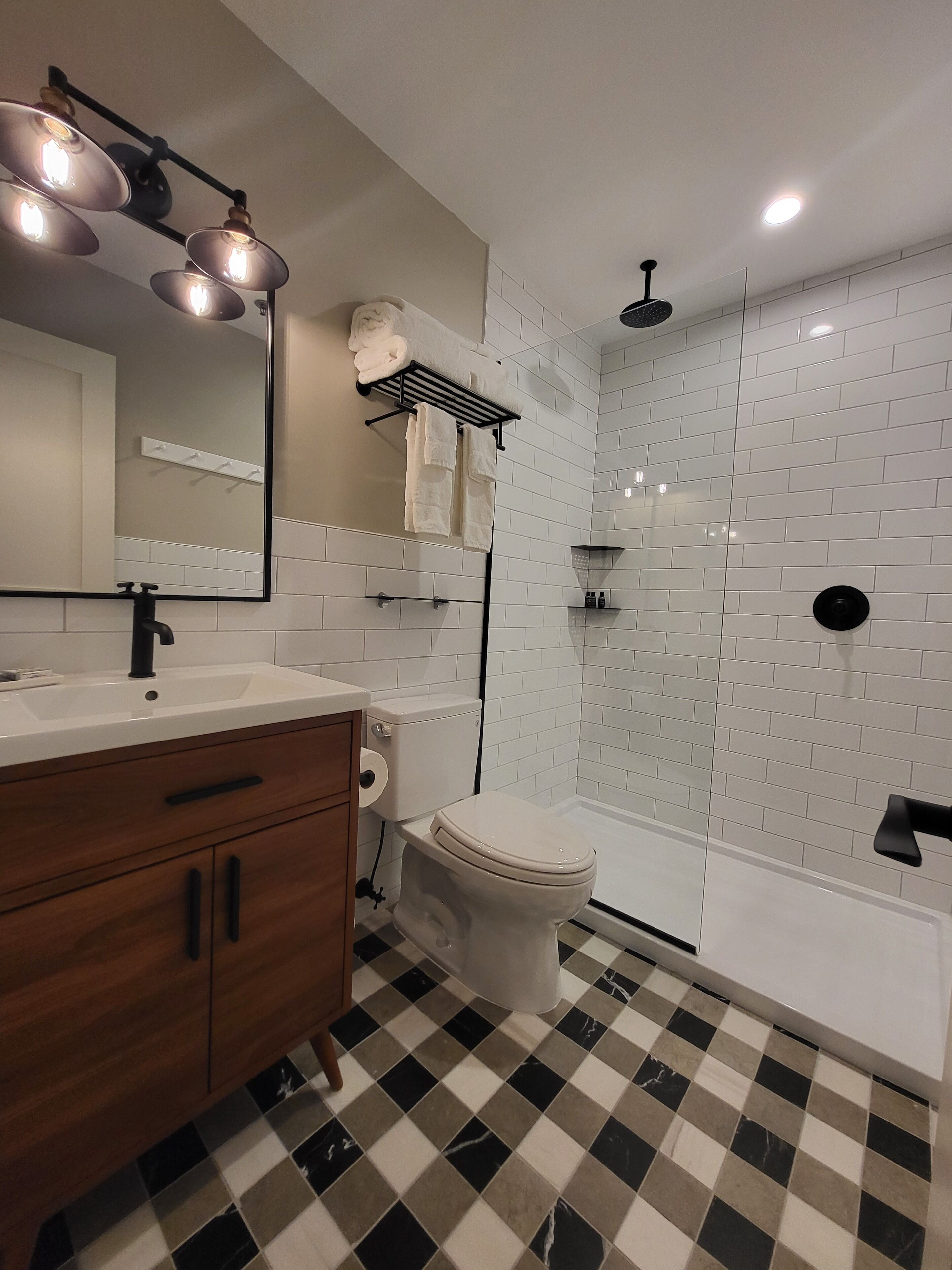Een moderne badkamer met een zwart-wit betegelde vloer, toilet, wastafel met spiegel en douche.