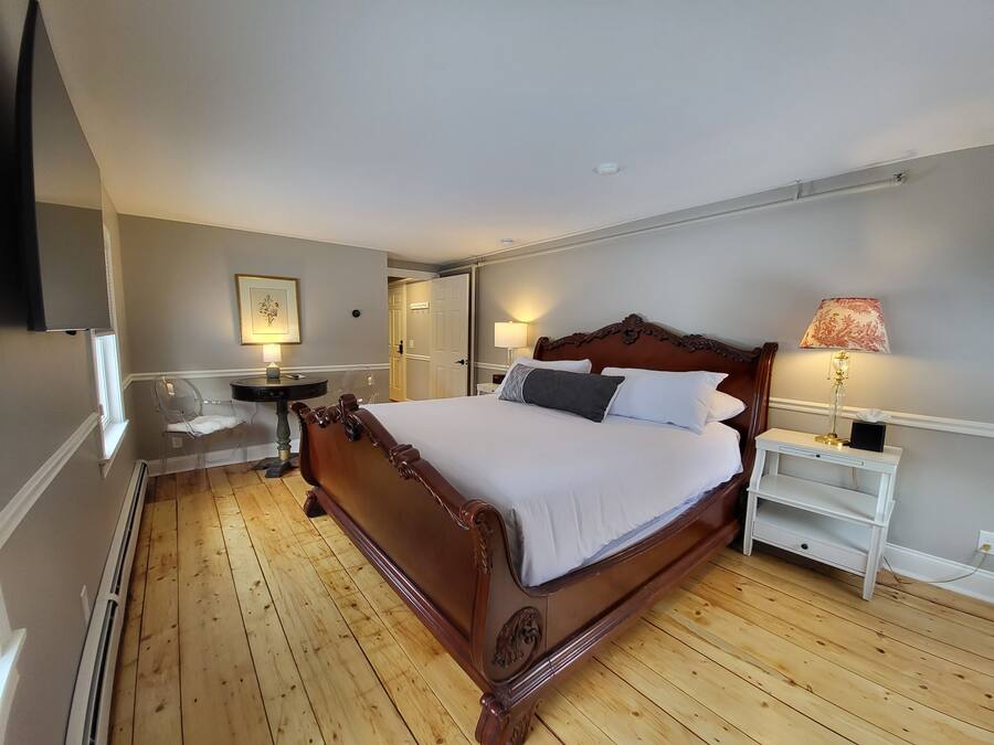 A bedroom with a wooden bed, a bedside table with a lamp, a chair, and a wardrobe.