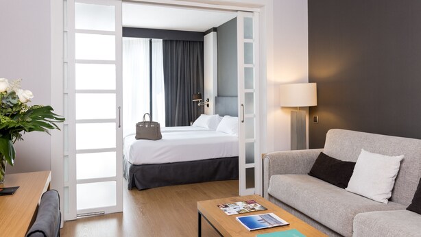 A hotel room with a bed, a sofa, a coffee table, and a lamp. - Guitart Grand Passage (Barcelona)