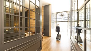 A modern hotel lobby with a wooden floor, large windows, and a person with a suitcase. - Guitart Grand Passage (Barcelona)