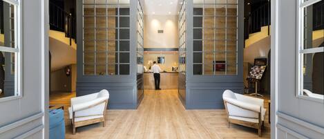 A hotel lobby with a central reception desk, two sofas, and a wooden floor.