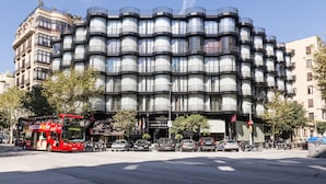 A multi-story building with a unique wavy facade, a red double-decker bus in front, and several cars parked along the street. - Guitart Grand Passage (Barcelona)