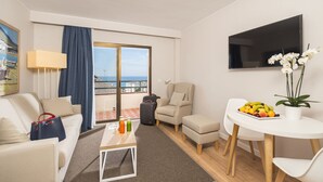 Une chambre d’hôtel moderne dotée d’un balcon, d’un canapé, d’une table basse avec des boissons, d’une télévision et d’un panier de fruits.