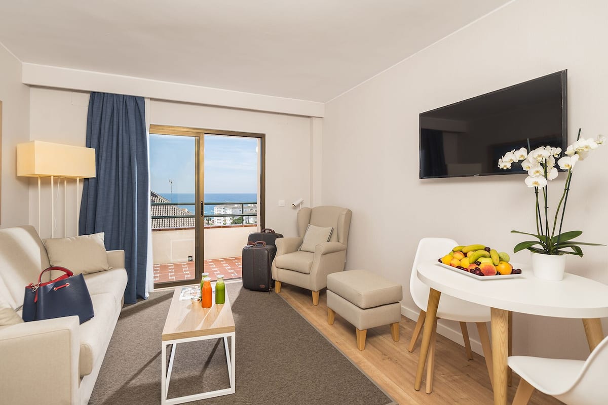 Een moderne hotelkamer met een balkon, een bank, een salontafel met drankjes, een televisie en een schaal fruit.