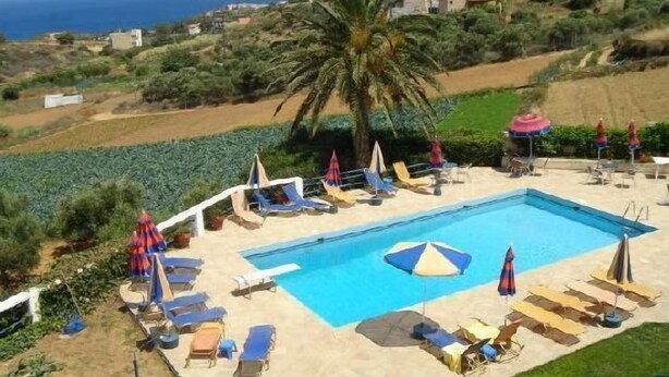 A pool area with lounge chairs and umbrellas, surrounded by greenery and a view of the sea and hills. - Esperides Apartments (Malevizi)