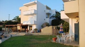 A modern building with a flat roof, multiple balconies, and a small outdoor seating area with tables and chairs. - Esperides Apartments (Malevizi)