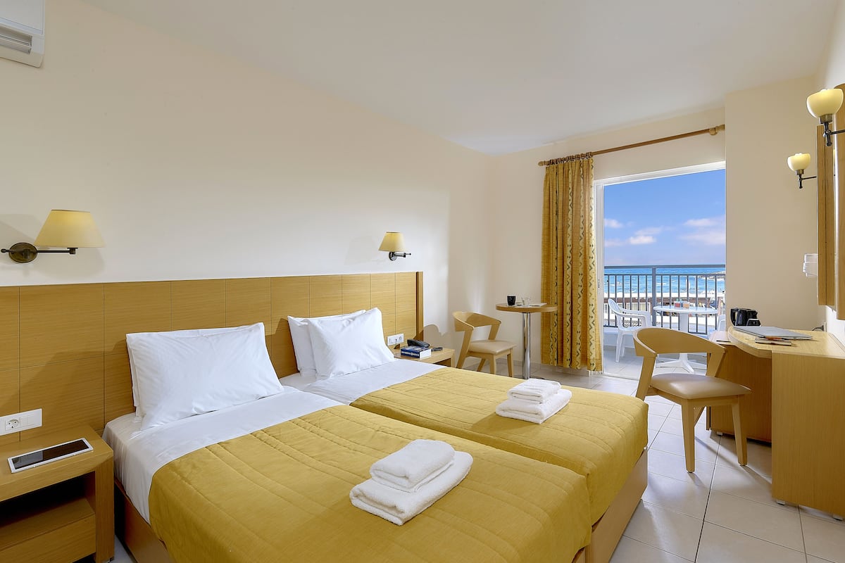 Habitación de hotel con dos camas, un escritorio, una silla y un balcón con vistas.